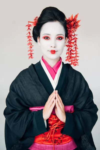 Lächelnd schöne Geisha im schwarzen Kimono mit grüßenden Händen auf weißem Hintergrund — Stockfoto