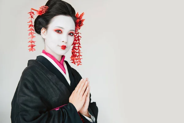 Smiling beautiful geisha in black kimono with greeting hands isolated on white with copy space — Stock Photo