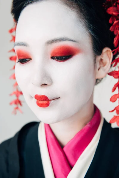 Vista de cerca de la hermosa geisha sonriente en kimono negro con flores rojas en el pelo aislado en blanco - foto de stock