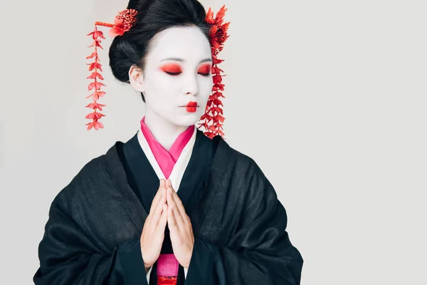 Красива гейша в чорному кімоно з червоними квітами у волоссі і вітальні руки ізольовані на білому — стокове фото