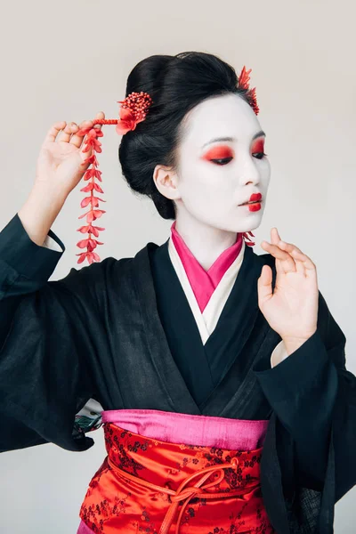 Schöne Geisha im schwarzen Kimono mit roten Blüten im Haar gestikuliert isoliert auf weiß — Stockfoto