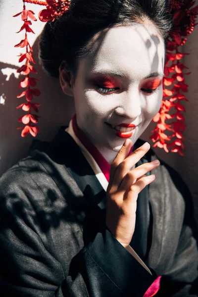 Porträt einer lächelnden schönen Geisha mit rot-weißem Make-up im Sonnenlicht mit Schatten — Stockfoto