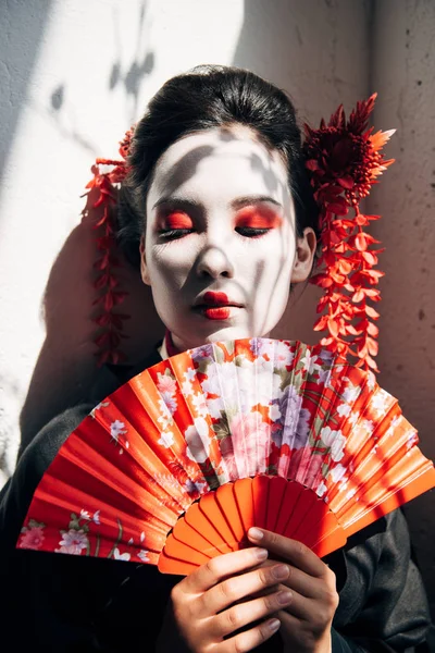 Портрет красивої гейші з червоно-білим макіяжем, що тримає вентилятор рук на сонячному світлі — стокове фото
