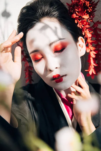 Fuoco selettivo di rami d'albero e geisha con trucco rosso e bianco e occhi chiusi alla luce del sole — Foto stock