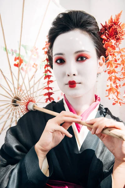 Красива гейша з червоно-білим макіяжем, що тримає парасольку на сонці — стокове фото