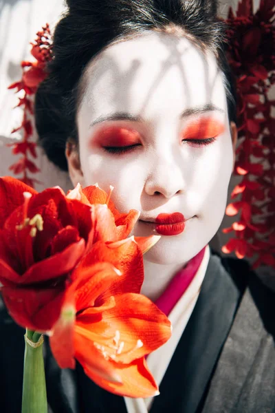 Portrait of beautiful geisha holding red flowers in sunlight — Stock Photo