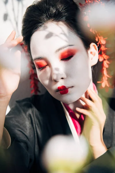Selective focus of tree branches and beautiful geisha with red and white makeup in sunlight — Stock Photo