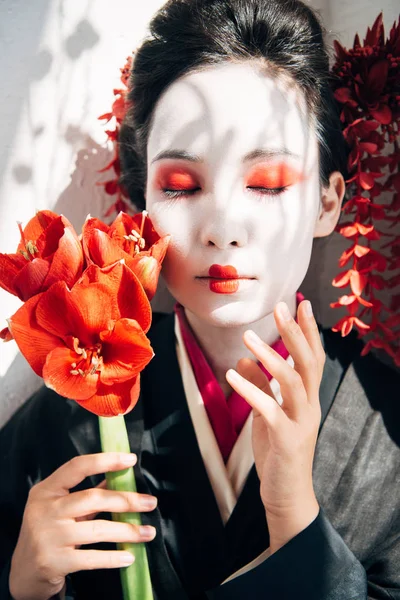 Portrait of beautiful geisha holding red flowers in sunlight — Stock Photo