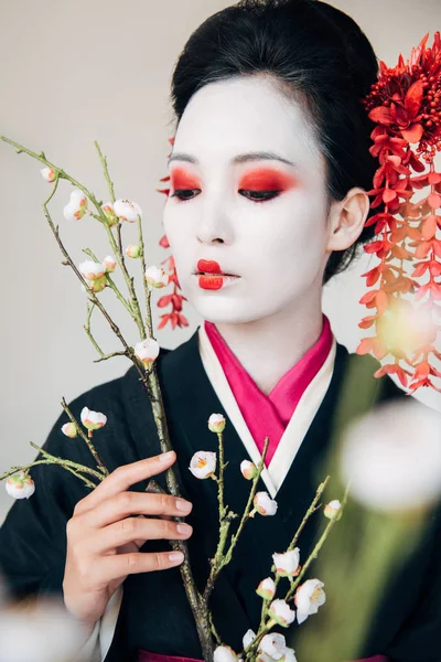 Selective focus of tree branches and beautiful geisha with red and white makeup isolated on white — Stock Photo