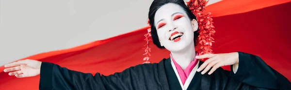 Happy beautiful geisha in black kimono with red cloth on background isolated on white, panoramic shot — Stock Photo