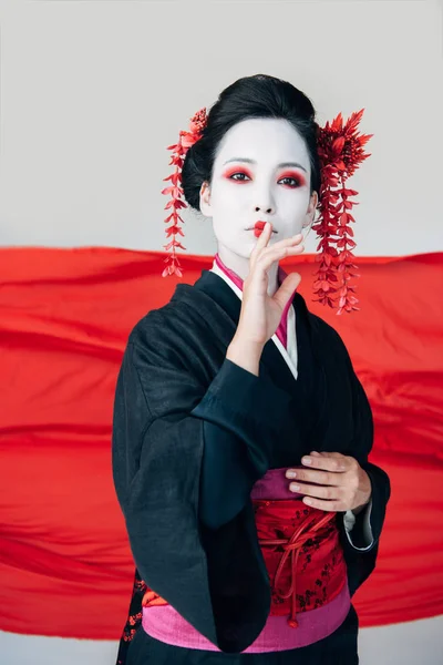 Красивая гейша в черном кимоно с красной тканью на заднем плане, показывающая знак 