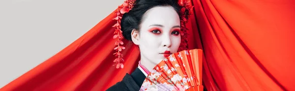 Hermosa geisha en kimono negro con ventilador de mano y tela roja sobre fondo aislado en blanco, plano panorámico - foto de stock