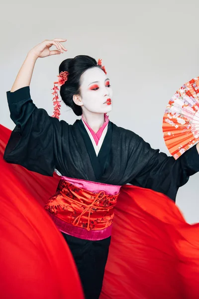 Geisha in black kimono with hand fan and red cloth on background dancing isolated on white — Stock Photo