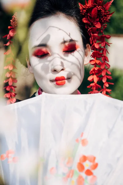 Selektiver Fokus der Äste und schöne lächelnde Geisha mit Sonnenschirm — Stockfoto