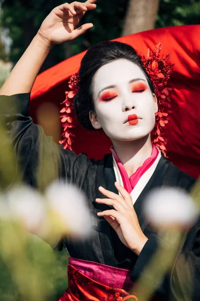 Selective focus of tree branches and dancing geisha with red cloth on background in sunlight — Stock Photo