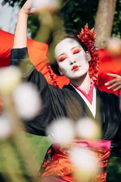 Selective focus of tree branches and beautiful dancing geisha with red cloth on background in sunlight — Stock Photo