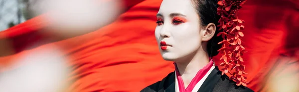 Selektive Fokussierung von Ästen und schöner Geisha mit rotem Tuch auf Hintergrund im Sonnenlicht, Panoramaaufnahme — Stockfoto