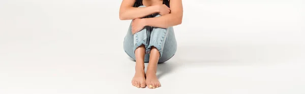 Panoramic shot of woman with barefoot sitting in blue jeans on white — Stock Photo