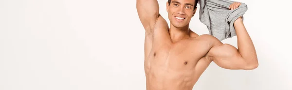 Tiro panorámico de hombre de raza mixta feliz desnudándose y mirando a la cámara en blanco - foto de stock