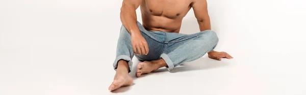 Panoramic shot of mixed race man in blue jeans sitting on white — Stock Photo