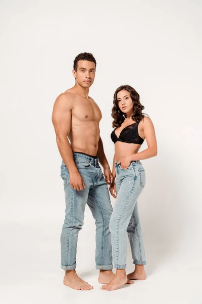 Sexy donna in pizzo reggiseno nero e jeans in piedi vicino muscolare uomo razza mista su bianco — Foto stock