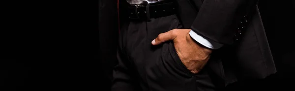 Panoramic shot of mixed race man standing with hand in pocket isolated on black — Stock Photo