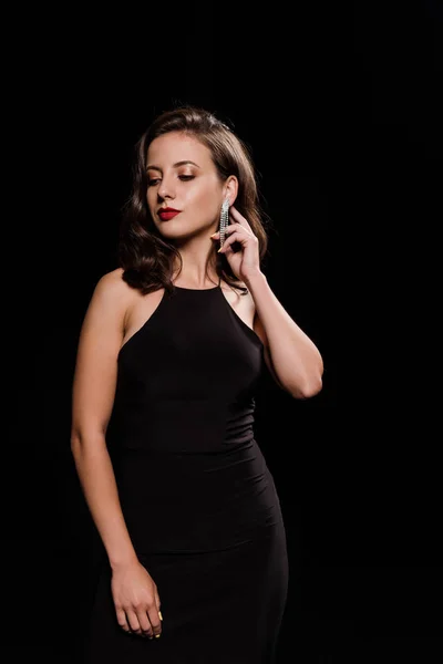 Elegante giovane donna toccante orecchino isolato su nero — Foto stock