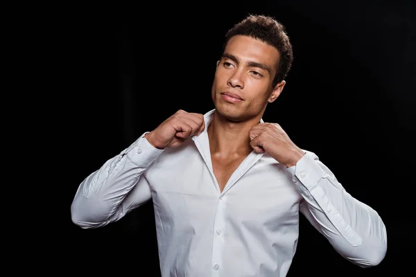 Handsome bi-racial man touching white shirt isolated on black — Stock Photo