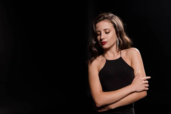 Attraente giovane donna in abito in piedi con le braccia incrociate isolato su nero — Foto stock