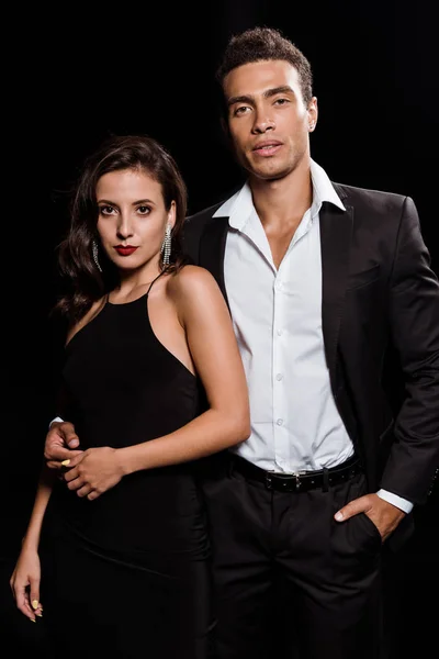 Handsome mixed race man standing with hand in pocket near attractive woman isolated on black — Stock Photo