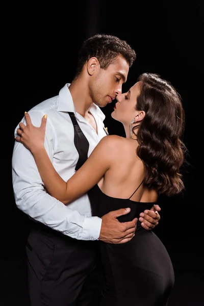 Handsome mixed race man embracing and looking at elegant woman isolated on black — Stock Photo