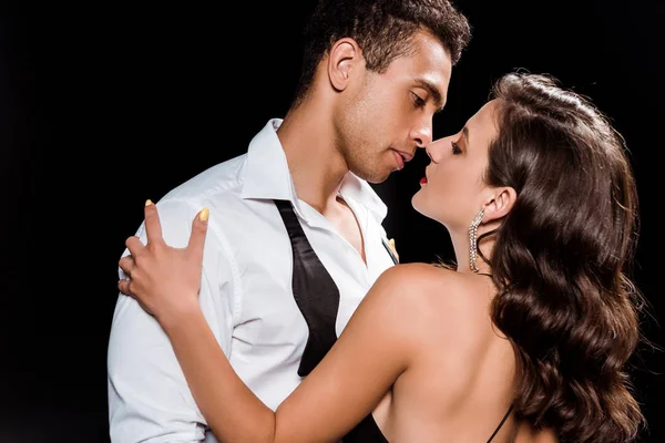 Guapo mestizo raza hombre abrazando y mirando elegante mujer aislado en negro — Stock Photo