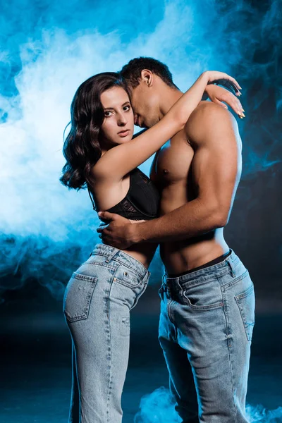Bi-racial man hugging sexy young woman on blue with smoke — Stock Photo