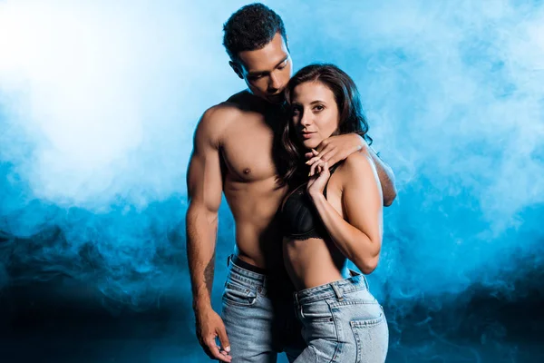 Handsome mixed race man holding hands with sexy girl on blue with smoke — Stock Photo