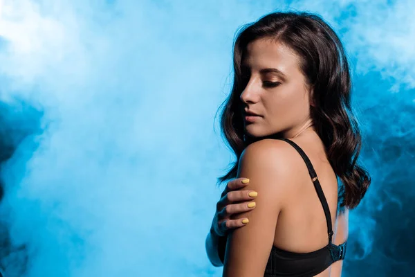 Приваблива жінка в мереживному чорному бюстгальтері, що стоїть на синьому з димом — стокове фото