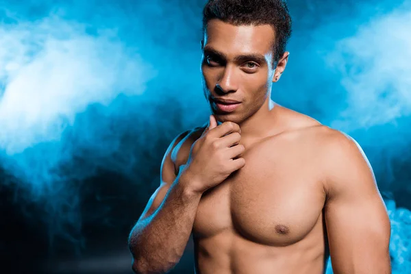 Sexy Mixed Race Mann berührt Gesicht auf blau mit Rauch — Stockfoto