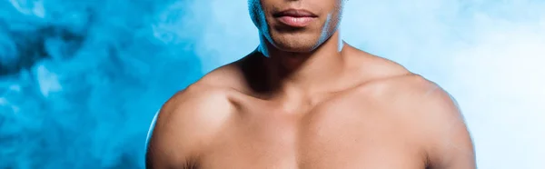 Панорамный снимок сексуального мужчины смешанной расы, стоящего на синем с дымом — стоковое фото