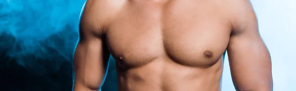 Panoramic shot of muscular mixed race man standing on blue with smoke — Stock Photo