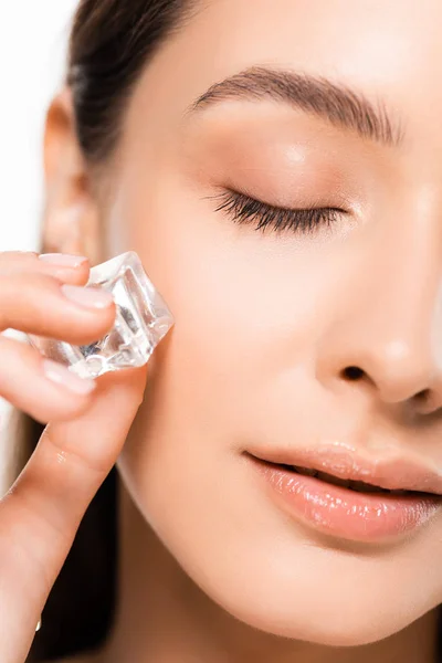 Close up view of beautiful brunette young woman with perfect skin and closed eyes holding ice cube isolated on white — Stock Photo