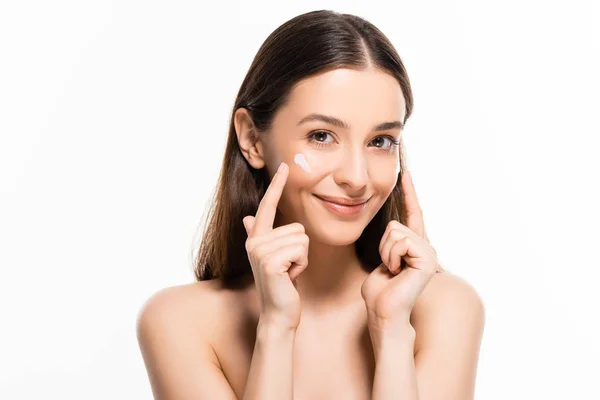 Hermosa mujer desnuda sonriente con la piel perfecta apuntando con los dedos a la crema cosmética en la cara aislada en blanco - foto de stock