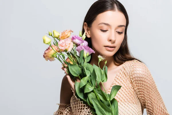 Hermosa mujer joven en malla beige sosteniendo ramo de flores de eustoma aisladas en gris con espacio de copia - foto de stock