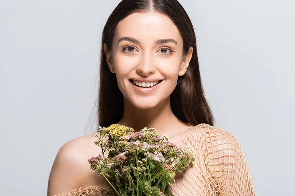 Schöne, glückliche Frau in beigem Mesh mit Wildblumen, die vereinzelt auf grau in die Kamera schauen — Stockfoto