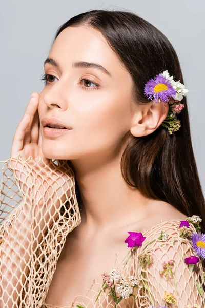 Beautiful model in mesh beige clothing with purple flowers touching face isolated on grey — Stock Photo