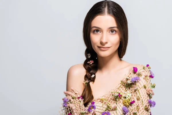 Hermosa joven con trenza en malla con flores silvestres de primavera aisladas en gris - foto de stock