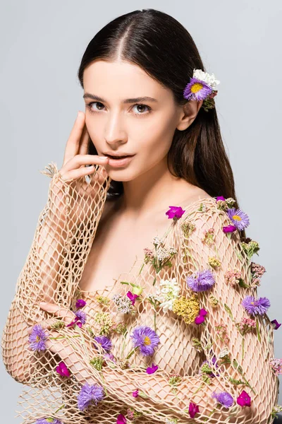 Beautiful woman in mesh beige clothing with purple flowers touching lips isolated on grey — Stock Photo