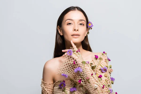 Hermosa chica en malla de ropa beige con flores púrpuras tocando la cara aislada en gris — Stock Photo
