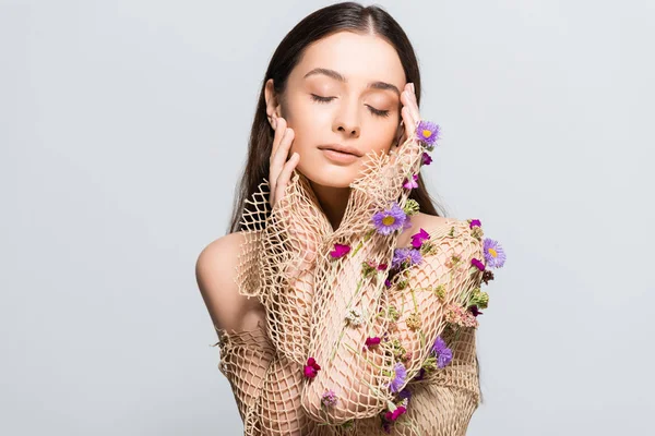 Beautiful woman with closed eyes in mesh beige clothing with purple flowers touching face isolated on grey with copy space — Stock Photo