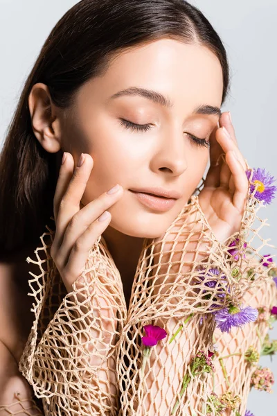 Beautiful girl  with closed eyes in mesh beige clothing with purple flowers touching face isolated on grey — Stock Photo