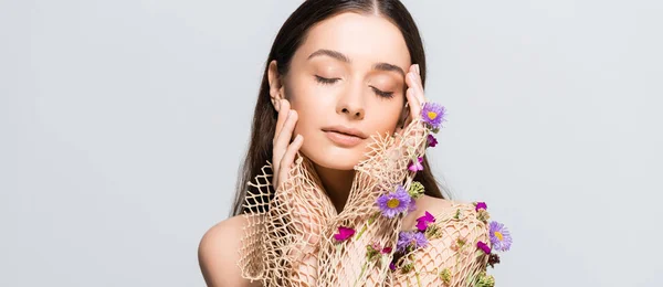 Beautiful woman with closed eyes in mesh beige clothing with purple flowers touching face isolated on grey — Stock Photo