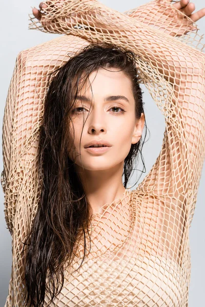 Красивая молодая женщина с мокрыми волосами в сетчато-бежевой одежде позирует изолированно на сером — стоковое фото